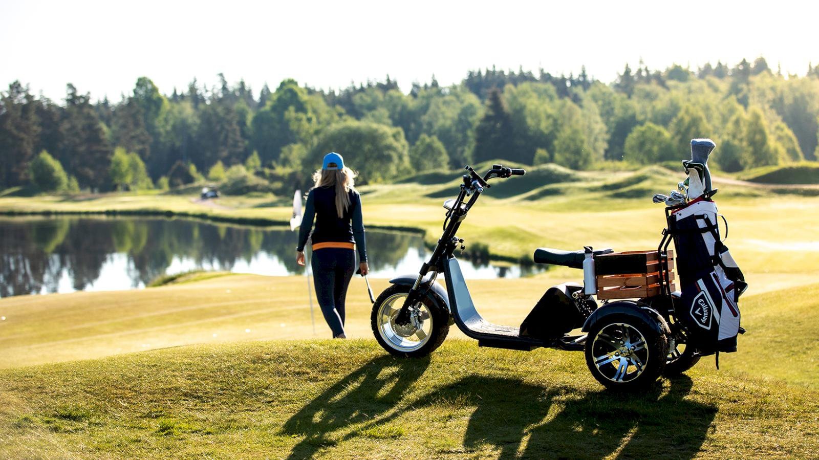 Scooter parkerad på golfbanan i kvällsljus, med spelare på väg mot greenen.